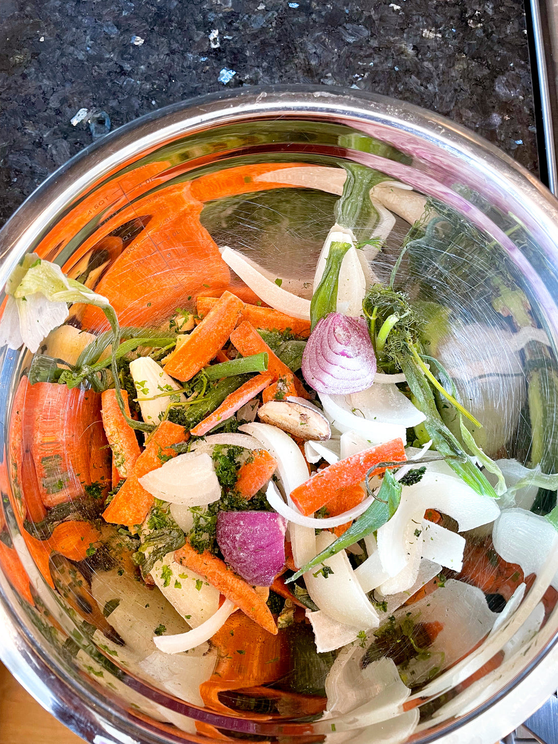 An overhead shot looking into a metal bowl. Inside the bowl are veggie scraps that are going to be used to make a veggie broth.